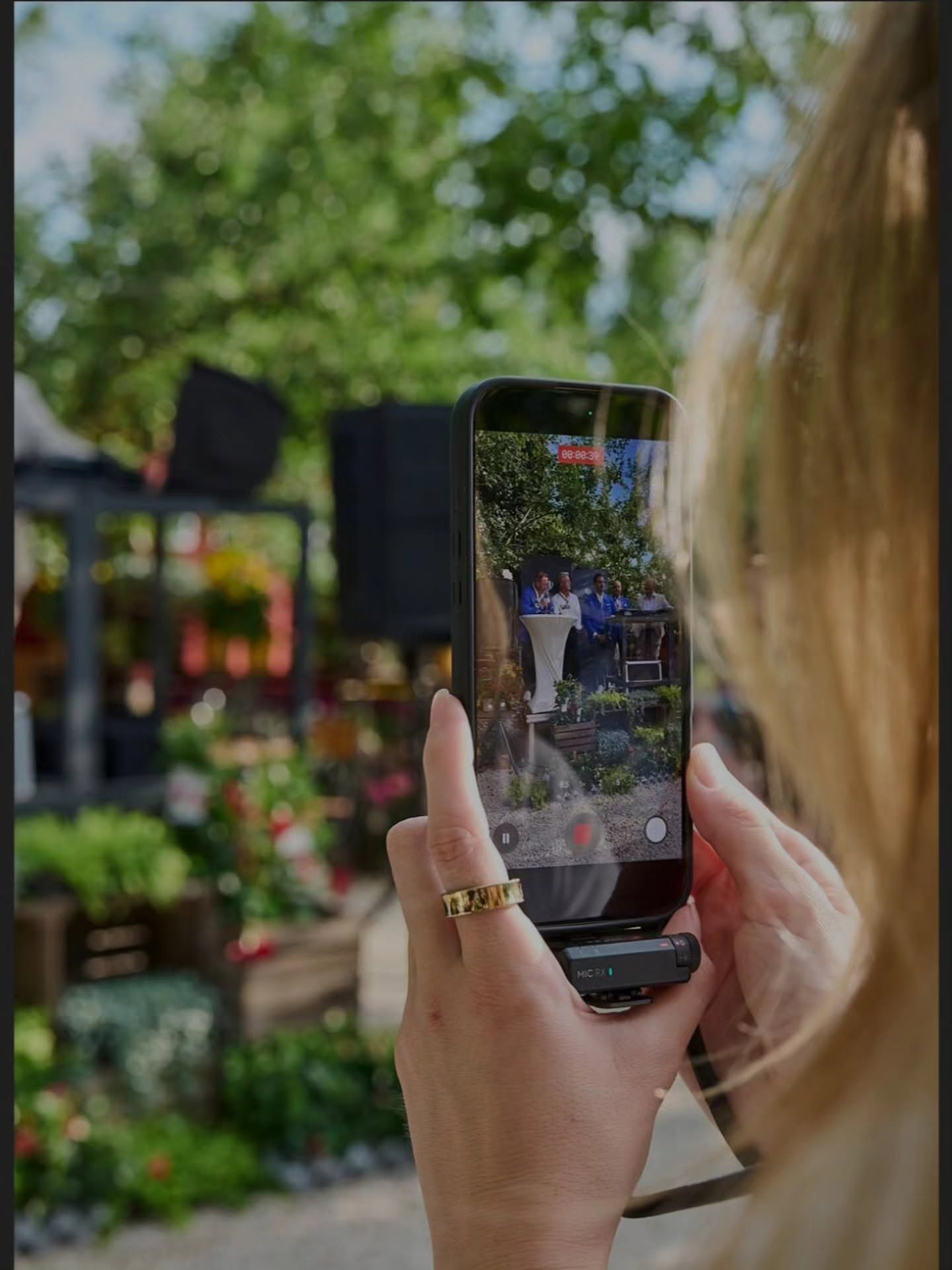 Gast hält einen Moment des Sommerfests mit dem Smartphone fest, im Hintergrund eine kleine Ansprache am Stehtisch